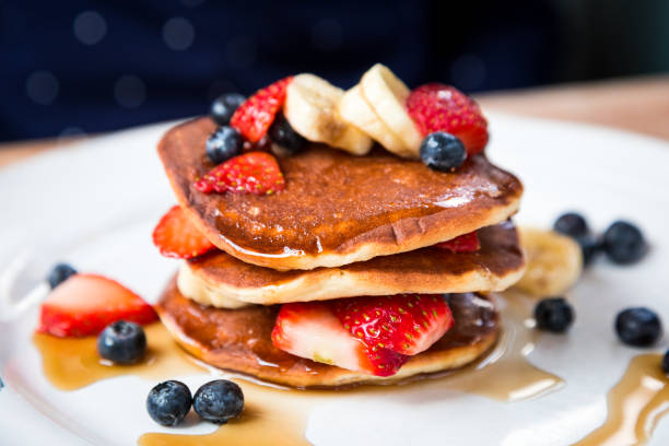 Maple syrup pouring from a glass jug over pancakes